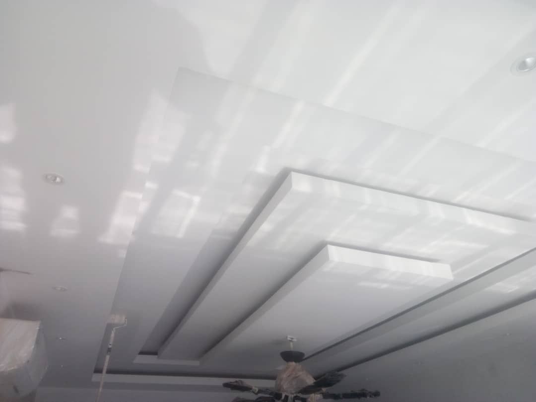 Modern white ceiling with rectangular recessed panels and built-in spotlights, illuminated by natural light.